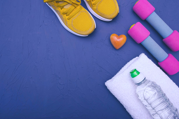 在家运动——蓝色背景上放着黄色运动鞋、哑铃、一瓶水和一条毛巾图片下载