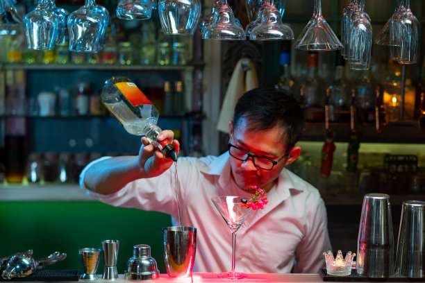 在夜总会吧台上用鸡尾酒杯加冰调制酒精饮料的酒保。图片下载