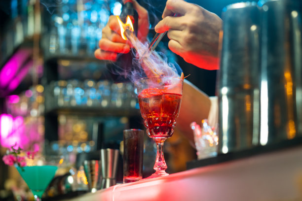 在夜总会吧台上用鸡尾酒杯加冰调制酒精饮料的酒保。图片下载