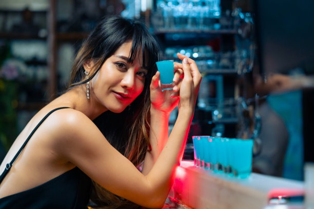 图为一名亚洲女子站在酒吧柜台边喝着马提尼酒。图片下载