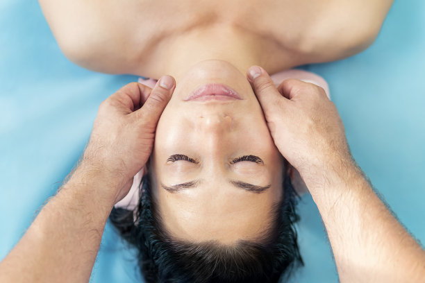 在按摩沙发上减压。一个熟睡的女人的脸特写在蓝色背景上。美丽的年轻女子正在接受面部按摩。图片下载