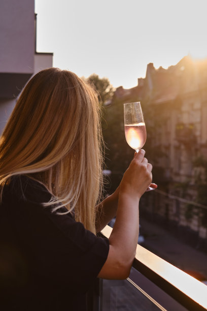 阳台上喝着玫瑰酒的女孩。喝点玫瑰红葡萄酒，享受这一刻。独自庆祝节日。轻松的生活方式。快乐的女人下班后休息。美丽的欧洲庭院图片下载