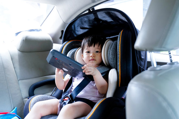 亚洲小女孩1 - 2岁在汽车座椅上系好安全带，抱着小熊平板玩具在车里，享受家庭度假。安全旅行宝贝概念。图片下载