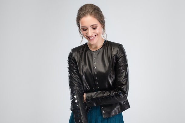 一个美丽的白人女子，身穿黑色皮夹克和深青绿色连衣裙，在浅灰色背景的工作室。为你的设计复制空间。图片下载