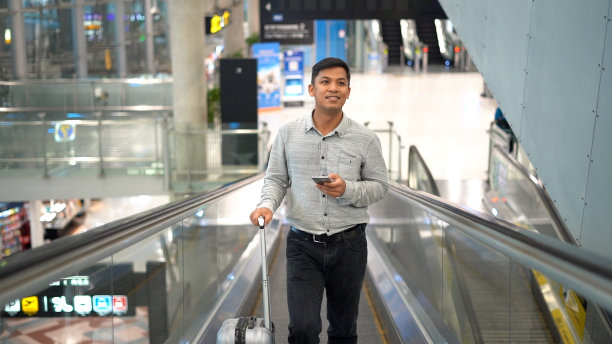 年轻人站在移动的人行道上使用智能手机。图片下载