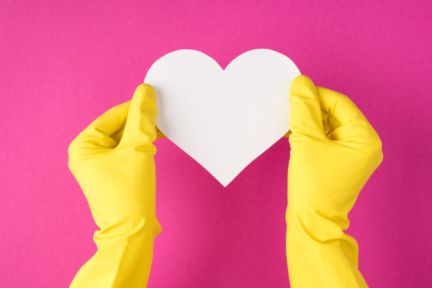 顶视图照片手在黄色手套持有白色的纸心在孤立的粉红色背景与copyspace图片下载