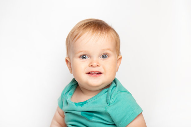 穿着绿色t恤的小男孩开心地笑着，看着被隔离在白色背景下的相机。儿童保育和养育的概念。图片下载