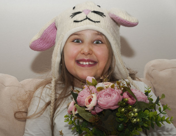有趣的微笑的小女孩长发戴着有趣的针织帽子与长兔子耳朵手持花束。复活节快乐，母亲节概念。图片下载