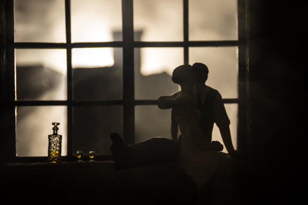 一个逼真的玩具屋客厅，在晚上有家具和窗户。一对浪漫的情侣坐在窗户上。艺术品桌子装饰与手工制作的现实的娃娃屋。有选择性的重点。图片下载