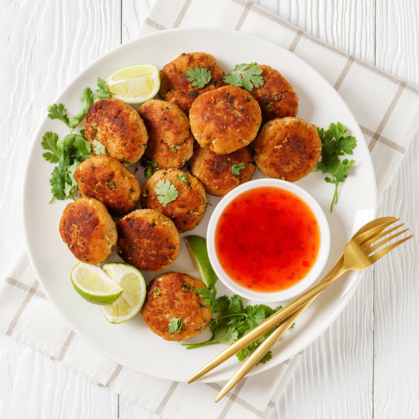 Tod man pla，甜辣椒酱的泰国鱼饼，放在白色的盘子里，配上酸橙和香菜，从上面俯瞰，平躺着图片下载