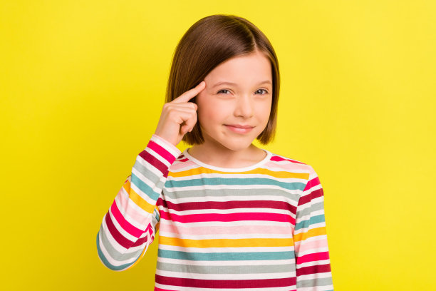照片中的小女孩在波波头发型保持手指靠近额头孤立的鲜艳的黄色背景图片下载