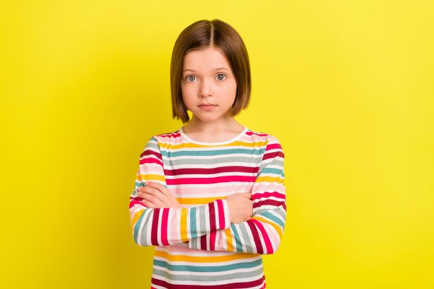 照片中的小女孩以波波头发型严肃，双手交叉孤立出鲜艳的黄色背景图片下载
