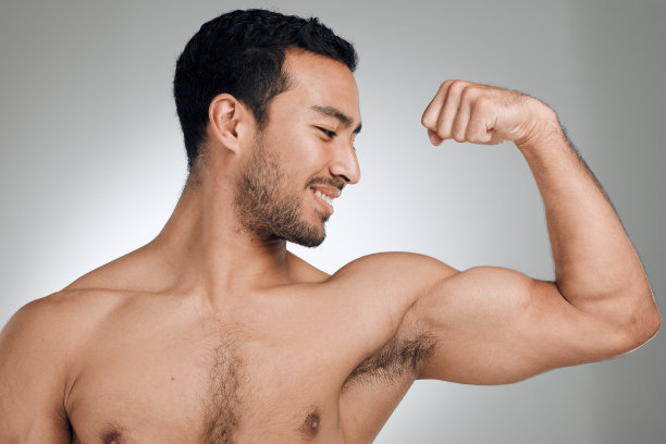 一名年轻男子站在灰色背景下展示肌肉图片下载