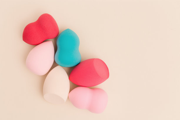 彩色化妆品美容海绵接近不同形式的米色背景与复制空间。俯视图，平躺。图片下载