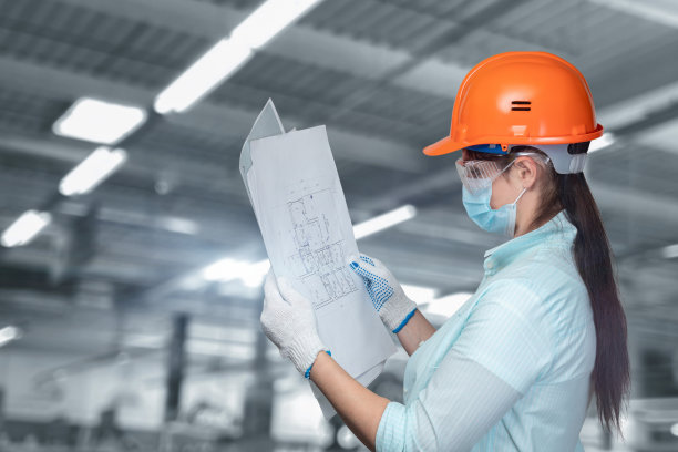 戴着防护头盔的工人在模糊的背景上看着一个技术项目。图片下载