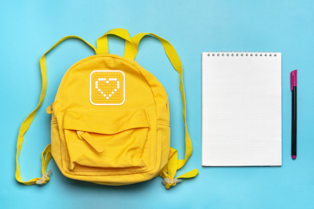 回到学校，教育理念。黄色背包里有学习用品-笔记本，笔孤立在蓝色背景上。前视图。复制空间平铺构图图片下载