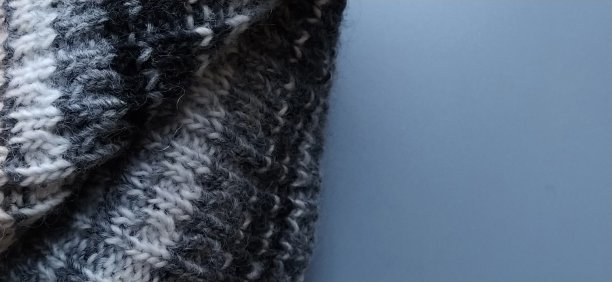 针织保暖产品，如灰色背景的围巾或帽子。多色纱线编织。冬装上有白色、灰色、棕色、米色和黑色的条纹和图案。图片下载