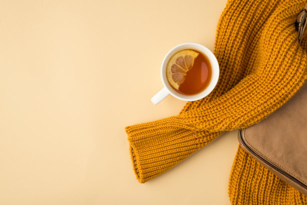 顶视图照片黄色毛衣米色皮革手袋和一杯茶与柠檬片在孤立的浅米色背景与copyspace图片下载