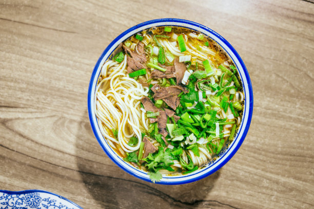 特写木桌上清汤牛肉面、蒜末、牛肉片图片下载