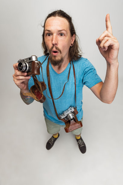 高角度的青年男子，摄影师，摄影师与复古相机孤立在灰色的工作室背景。职业概念，工作，有趣的模因情绪图片下载