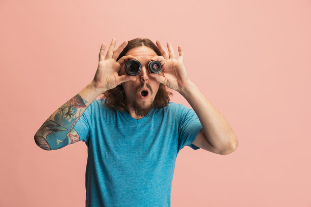 年轻男子的肖像，摄影师，摄影师与相机镜头有乐趣孤立在粉红色的工作室背景。职业概念，工作，有趣的模因情绪图片下载