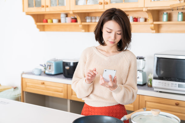 亚洲美女看智能手机，厨房图片下载