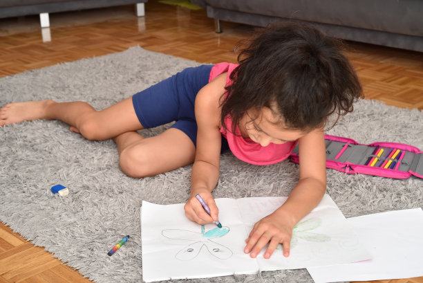 一个年轻的女孩躺在地毯上给她的画上色图片下载