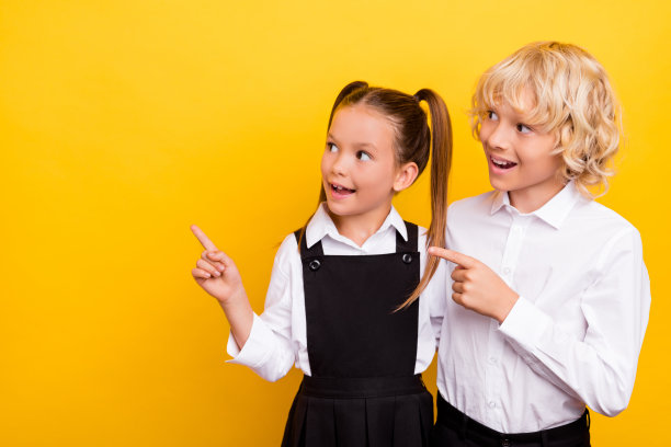 好奇的小学生照片，直指空白处，穿校服孤立黄色背景图片下载