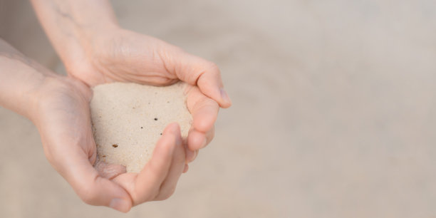 女人的双手捧着白色的沙滩沙子。图片下载