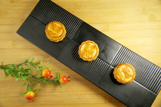 黑色盘子上放着三个月饼，上面有中文文字:榴莲、蛋黄、枣子和草莓，俯视图图片下载