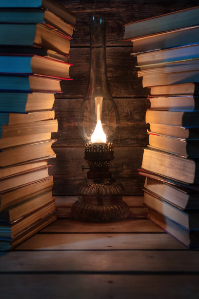 一盏旧煤油灯在两堆高高的书中间发光。背景。图片下载