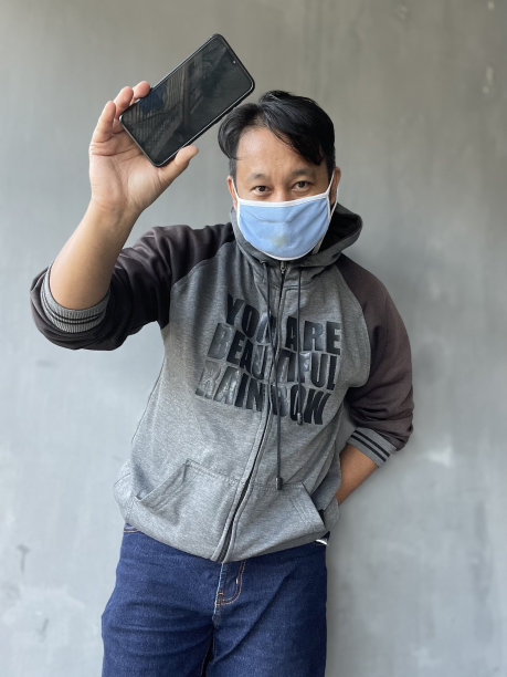 一名男子拿着智能手机站在浅灰色的墙前图片下载