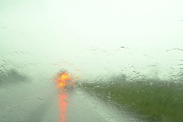 通过被雨覆盖的汽车挡风玻璃看到的散焦交通。关注雨滴这是在秋天图片下载