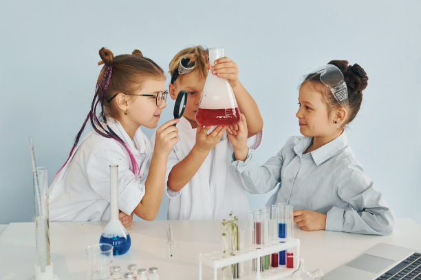 拿着试管站在桌子旁边。穿着白大褂的孩子们用仪器在实验室里扮演科学家图片下载
