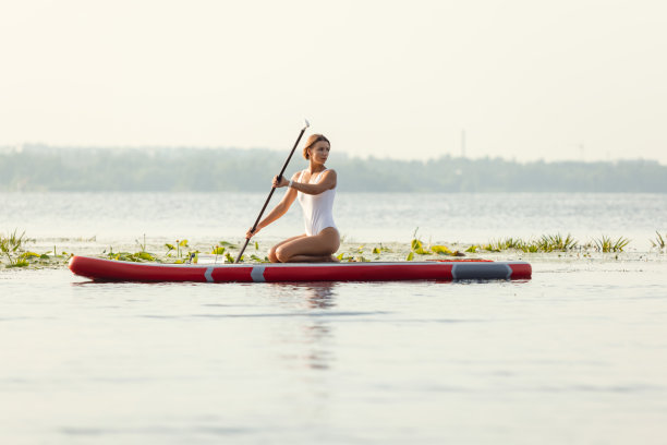 一个年轻的白种人美丽苗条的女孩日光浴在夏天的晚上在河上桨板，SUP独自。积极生活、运动、休闲的活动理念图片下载