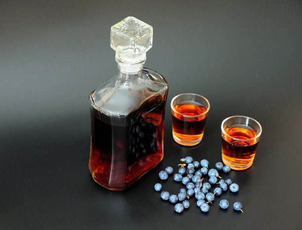 自制蓝莓利口酒，玻璃瓶和两个玻璃杯与饮料和成熟的浆果在黑色背景。图片下载