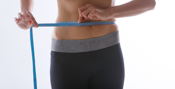 运动锻炼的结果:白色背景下一个结实的腹部特写。这女孩用一根厘米长的带子量腰围。饮食的影响图片下载