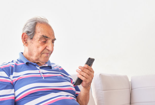 年长的黑发灰发男子身穿条纹衬衫，手里拿着一部背景浅色的智能手机图片下载