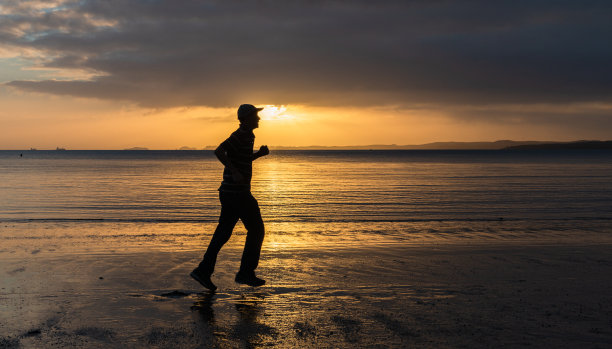 日出时一个男人在沙滩上奔跑的剪影图片下载