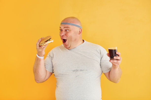 快餐。有趣的超重男子在运动头领带是在黄色背景图片下载