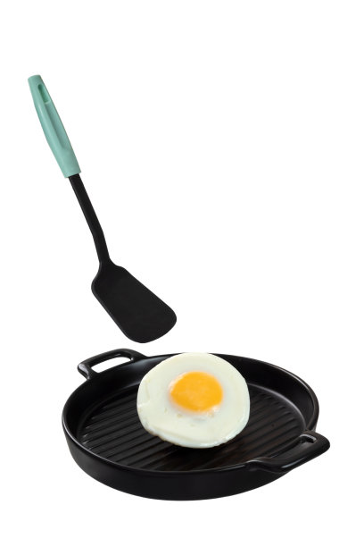 一个煎蛋和一个硅胶刮刀悬浮在黑色陶瓷上菜锅上。图片下载