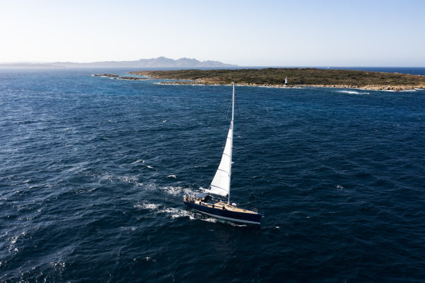 在阳光明媚的日子里，一艘帆船在蓝色的海面上航行，令人惊叹的鸟瞰图。意大利撒丁岛的翡翠海岸。图片下载
