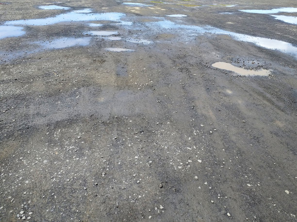 砾石路的背景与泥坑和雨水。抽象的纹理。土路上的脏水坑。法属西印度群岛沙地道路上的泥、坑洞和水坑。图片下载