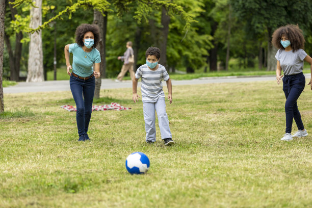 一个戴着面具的快乐非裔美国家庭正在草地上玩足球。图片下载