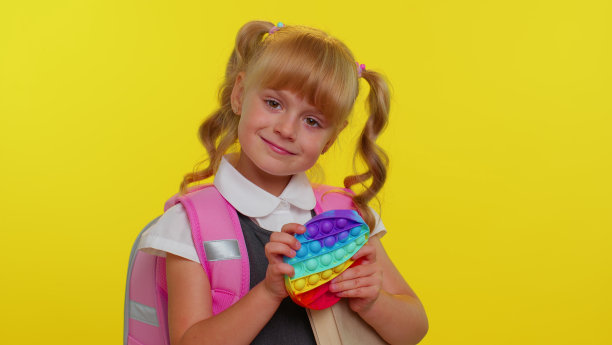 快乐的小学生女孩玩着pop it感官抗压力玩具，小朋友按上软绵绵的泡泡游戏图片下载