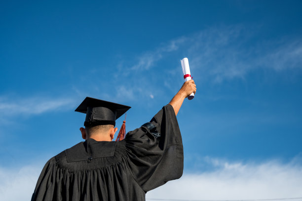 男子的后视图在空中举起证书和帽子，毕业日的天空背景图片下载