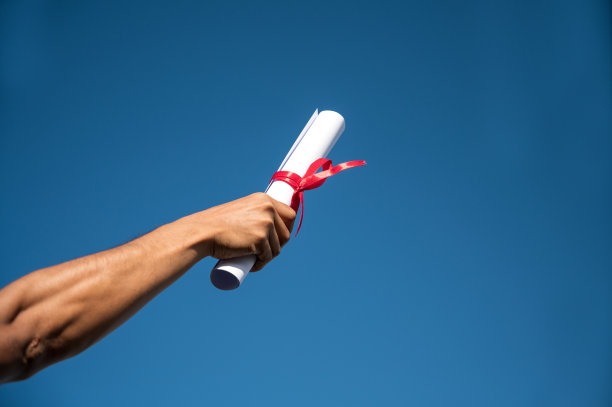 男子的后视图在空中举起证书和帽子，毕业日的天空背景图片下载