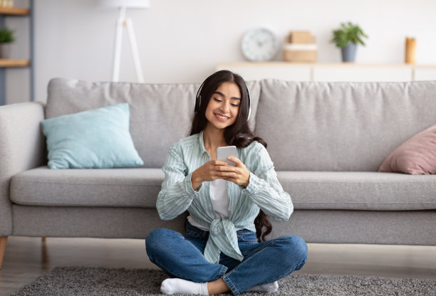 戴着耳机用手机听音乐的印度年轻女子坐在地板上图片下载