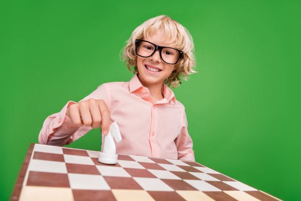 照片欢快的年轻快乐的正男孩手握图形棋盘孤立在绿色的背景图片下载