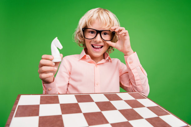 照片正面开朗快乐的男孩手牵马图象棋微笑孤立在绿色背景上图片下载